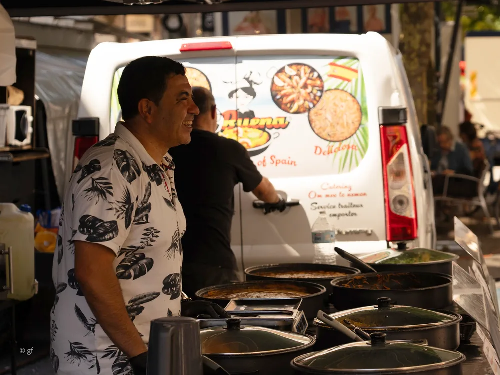 Een van onze koks lacht achter de paellapannen op de markt in Leuven